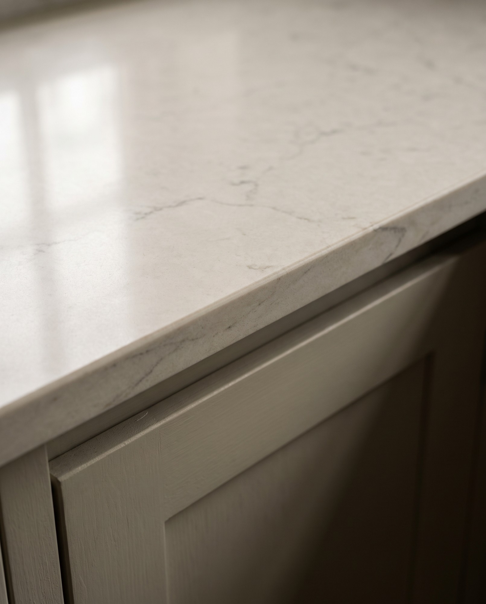 Close-up of a pale stone worktop edge above a painted shaker cabinet