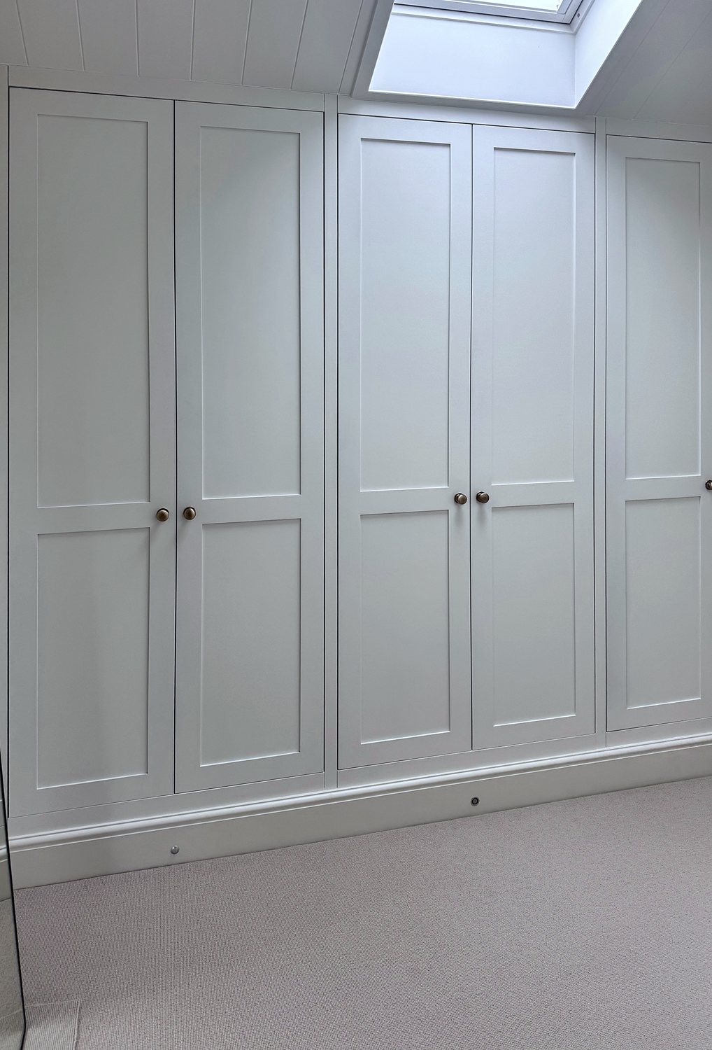 Painted wardrobes fitted into the eaves beneath a roof light, scribed to the slope of the ceiling