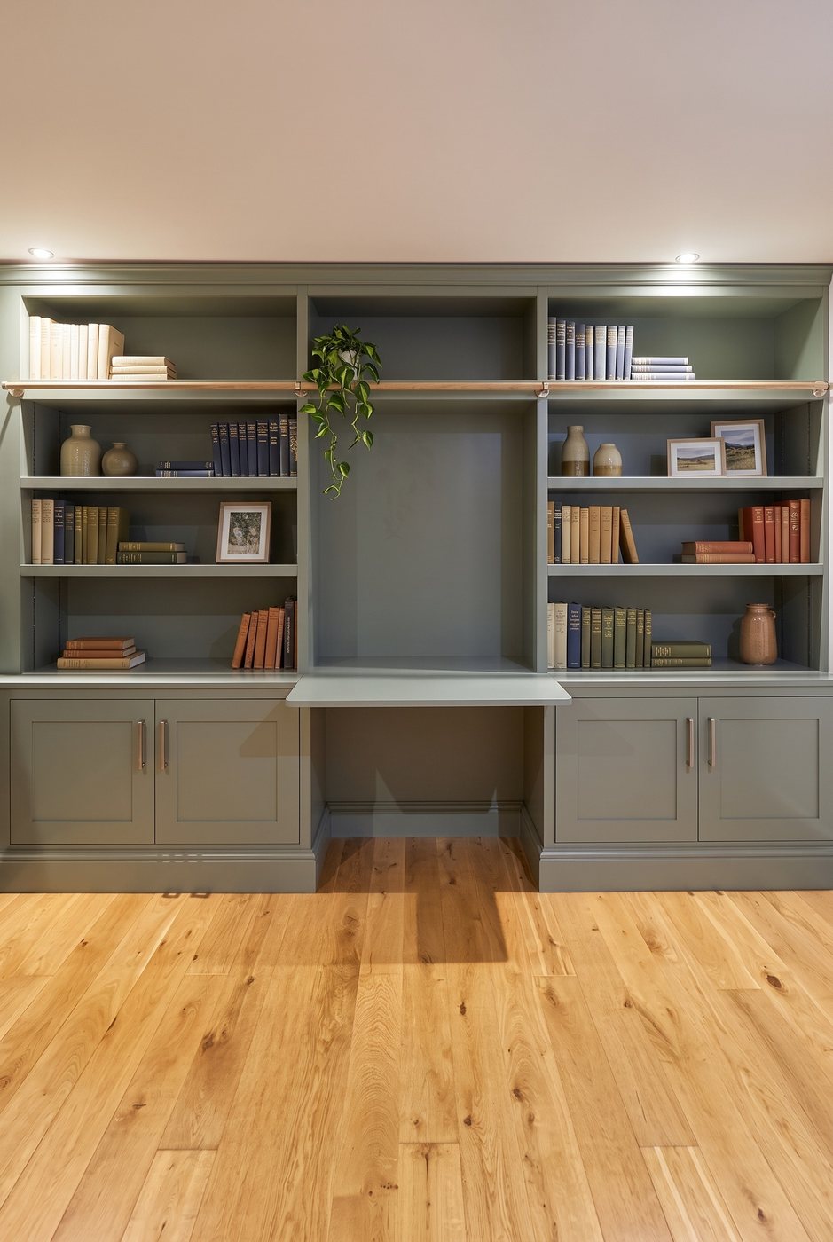 Sage-green shelving either side of a fold-out desk, with panelled cupboards below